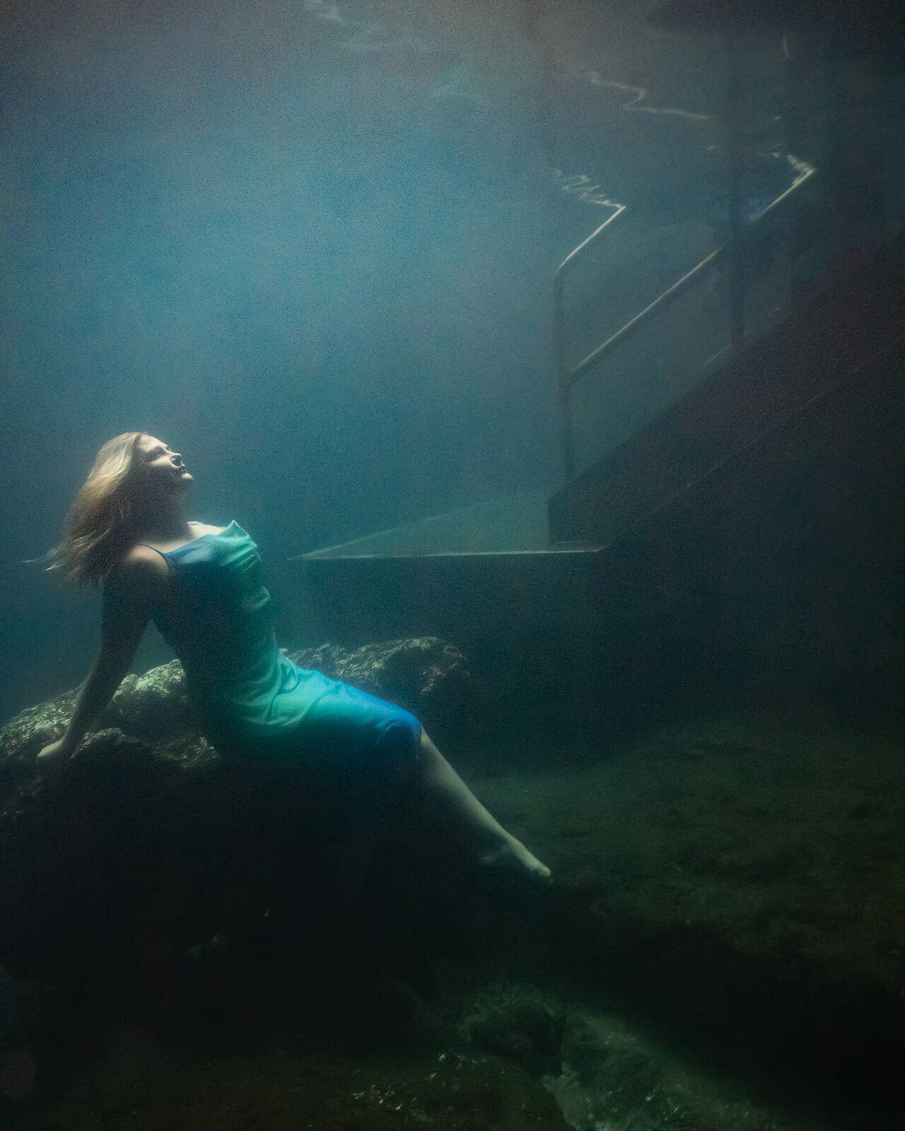 Mermaid seated on a rock in soft blue light inside the Devil's Den cavern